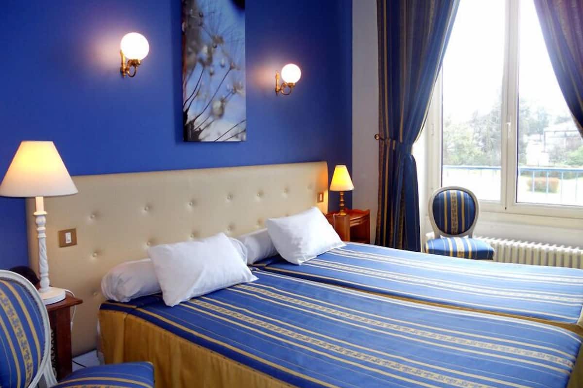 Quarto de hotel com uma cama grande, duas luminárias de cabeceira, uma janela com cortinas e uma cadeira.
