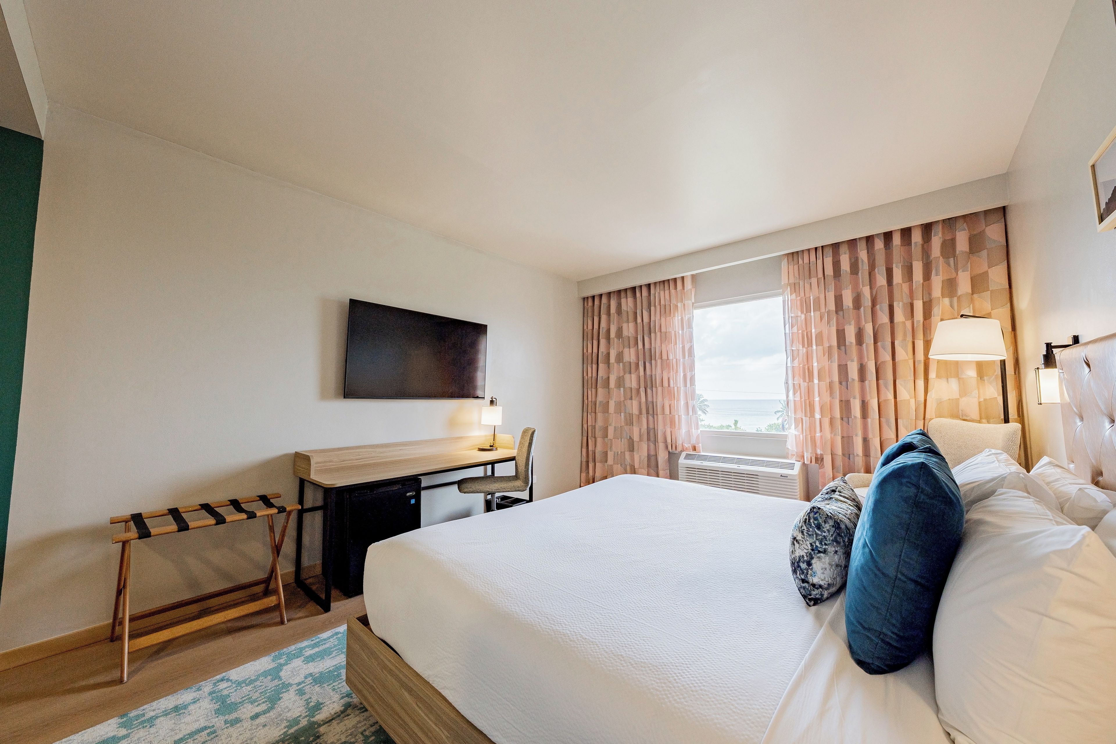 A hotel room with a bed, a desk, a chair, a TV, and a window with curtains.
