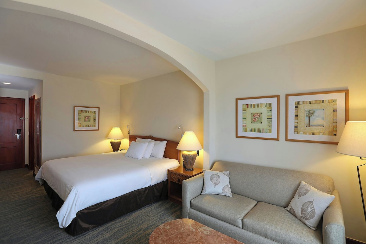 A hotel room with two beds, a sofa, and a small table. There are framed pictures on the wall and lamps on the nightstands.