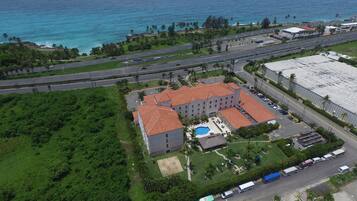 Vista aérea de um hotel com piscina, vários estacionamentos e uma estrada com veículos.
