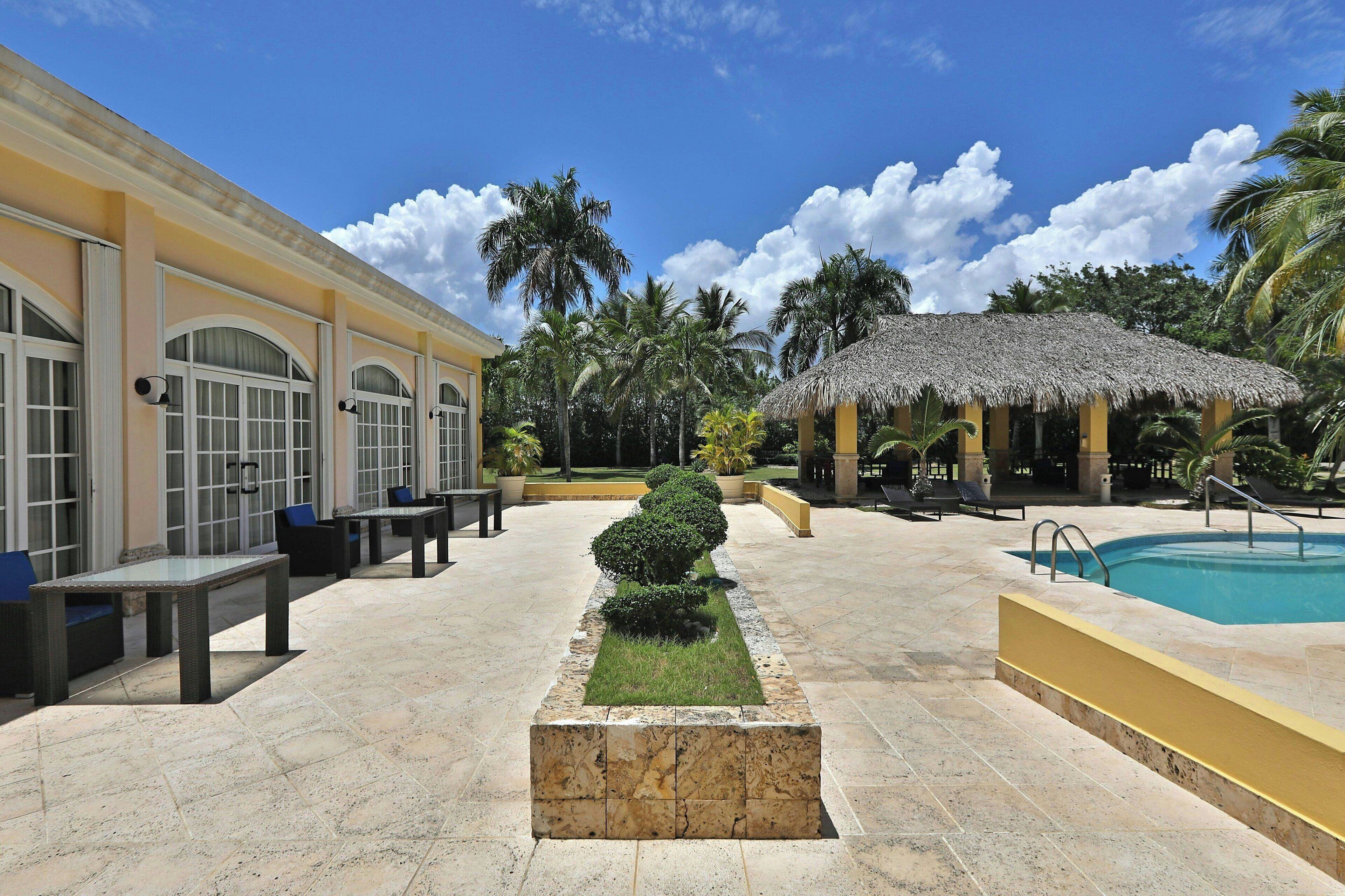 Um pátio com piscina, área de estar ao ar livre e estrutura coberta de palha.
