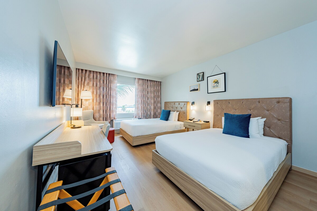 Habitación de hotel con dos camas, un escritorio, una silla y un televisor.