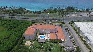 An aerial view of a hotel with a swimming pool, multiple parking lots, and a view of the ocean. - Four Points by Sheraton Santo Domingo (Boca Chica)