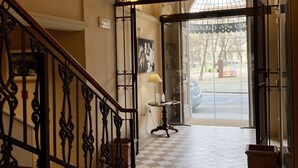 A hotel entrance with a checkered floor, a staircase with ornate railings, and a glass door leading outside.