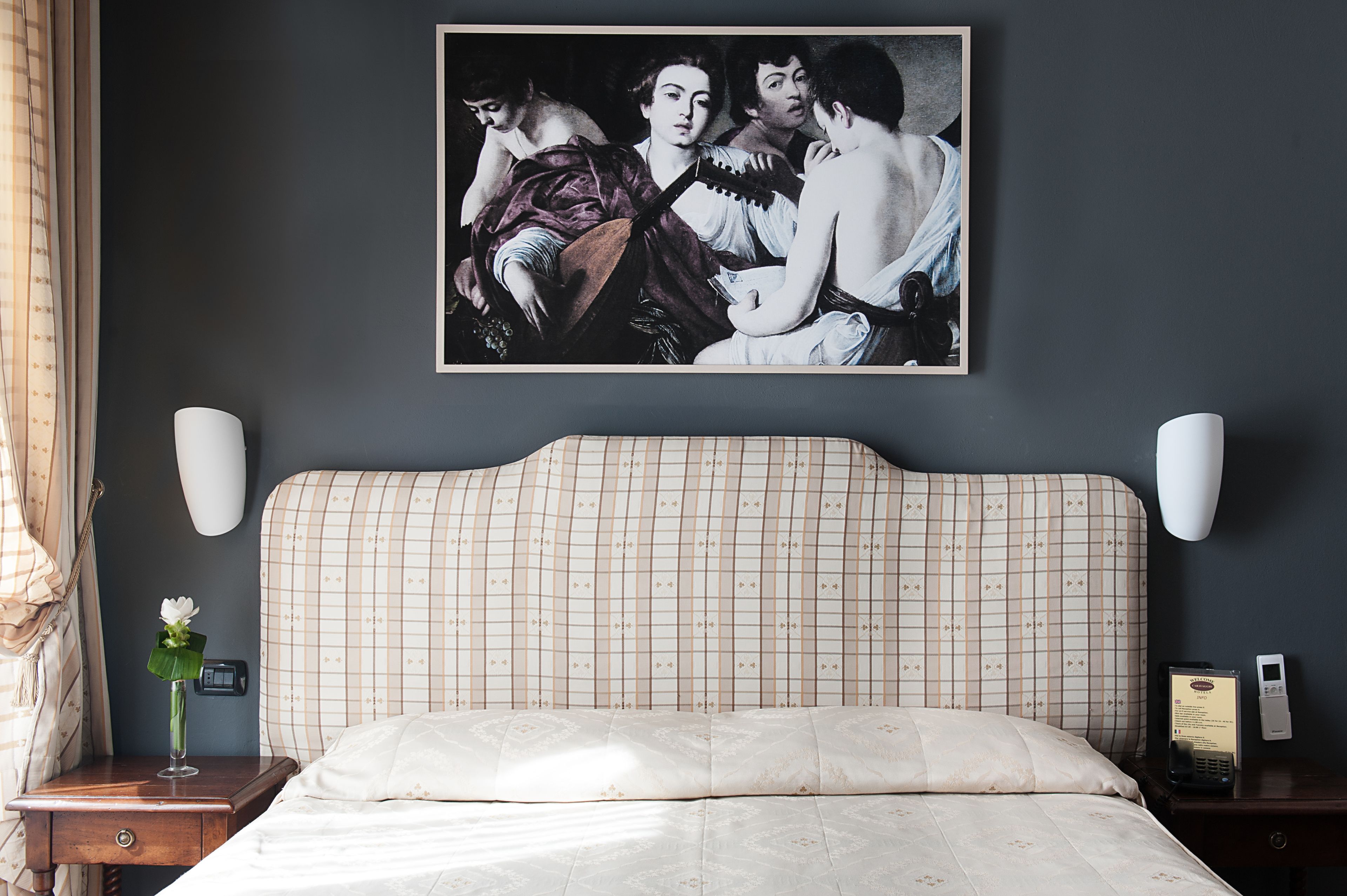 Una camera d'albergo con un letto grande, un comodino con una lampada, un telefono e un quadro appeso al muro.