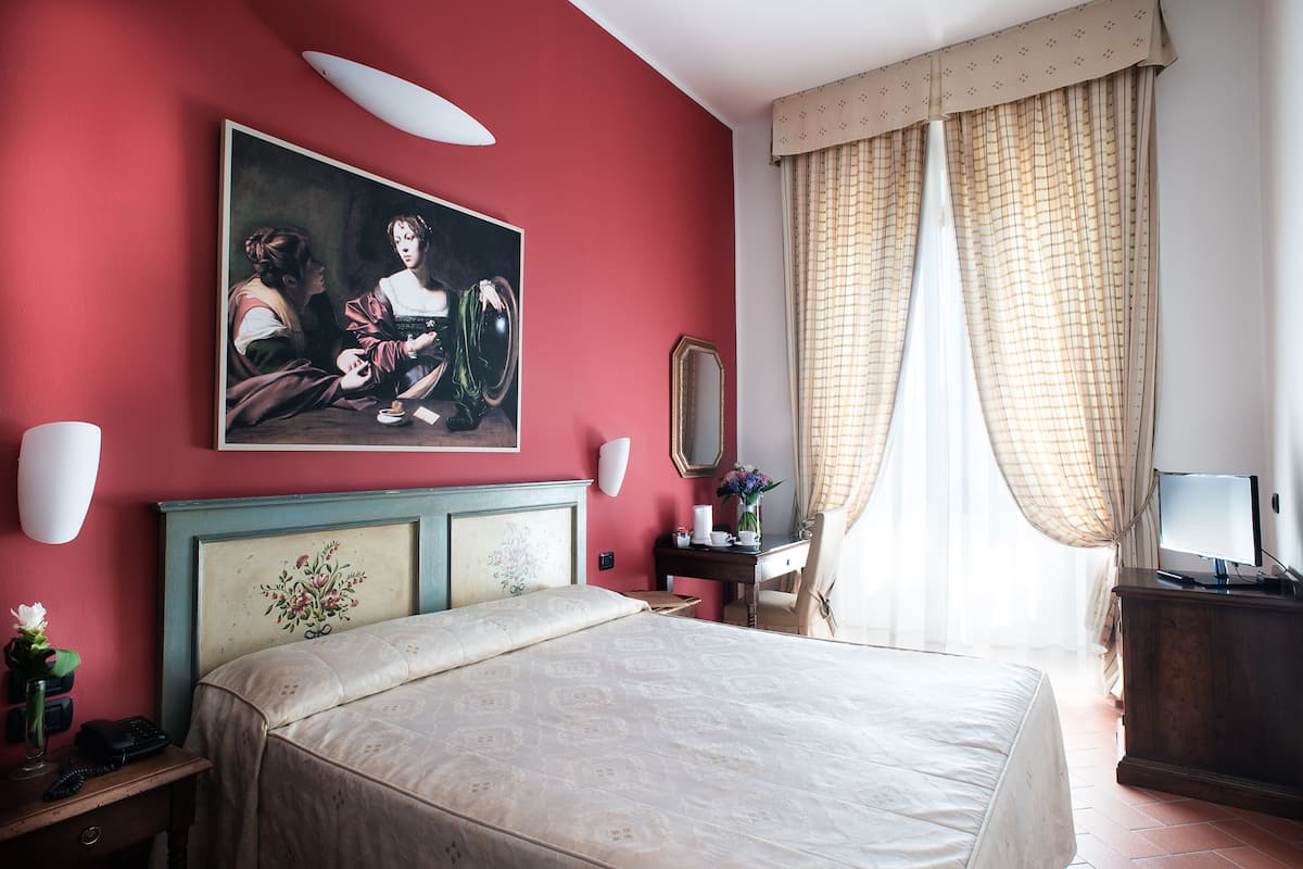 Habitación de hotel con una cama grande, un cuadro en la pared, un escritorio con espejo y un televisor.