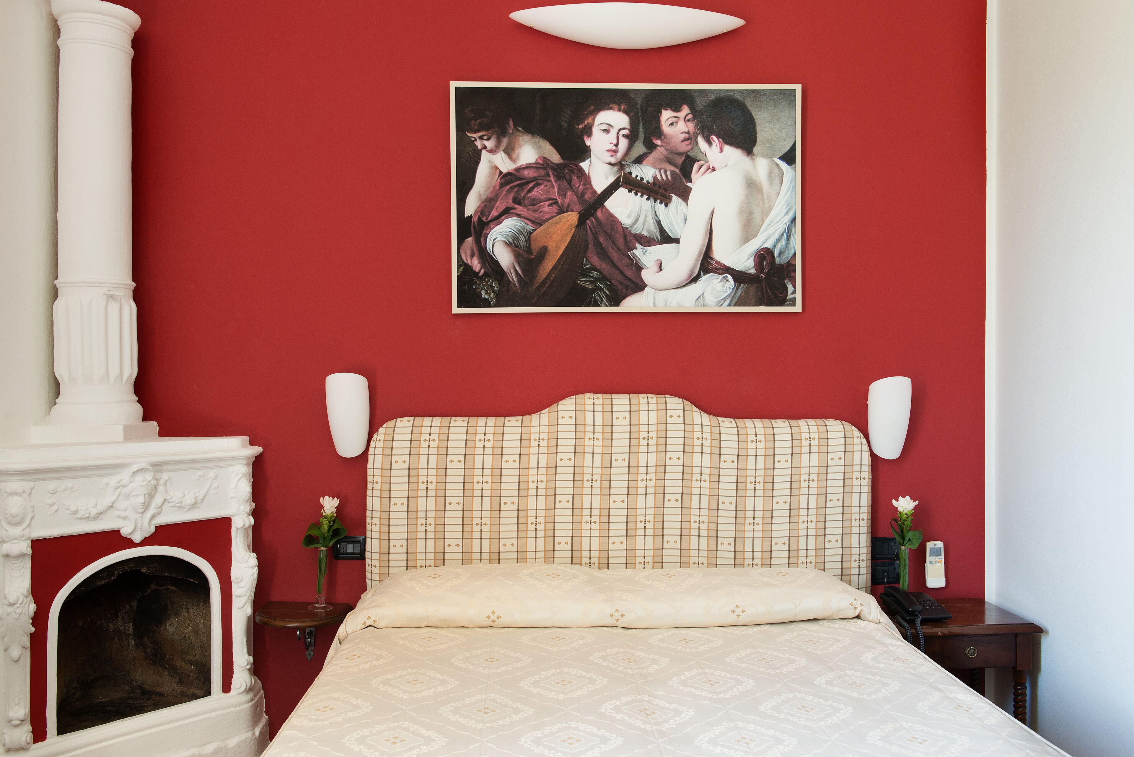 Une chambre avec un mur rouge, une cheminée classique, un lit avec une tête de lit à motifs et un tableau au-dessus du lit.