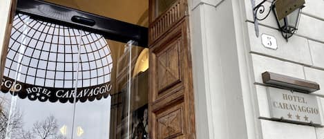 The entrance of Hotel Caravaggio with a wrought iron gate and a glass door.