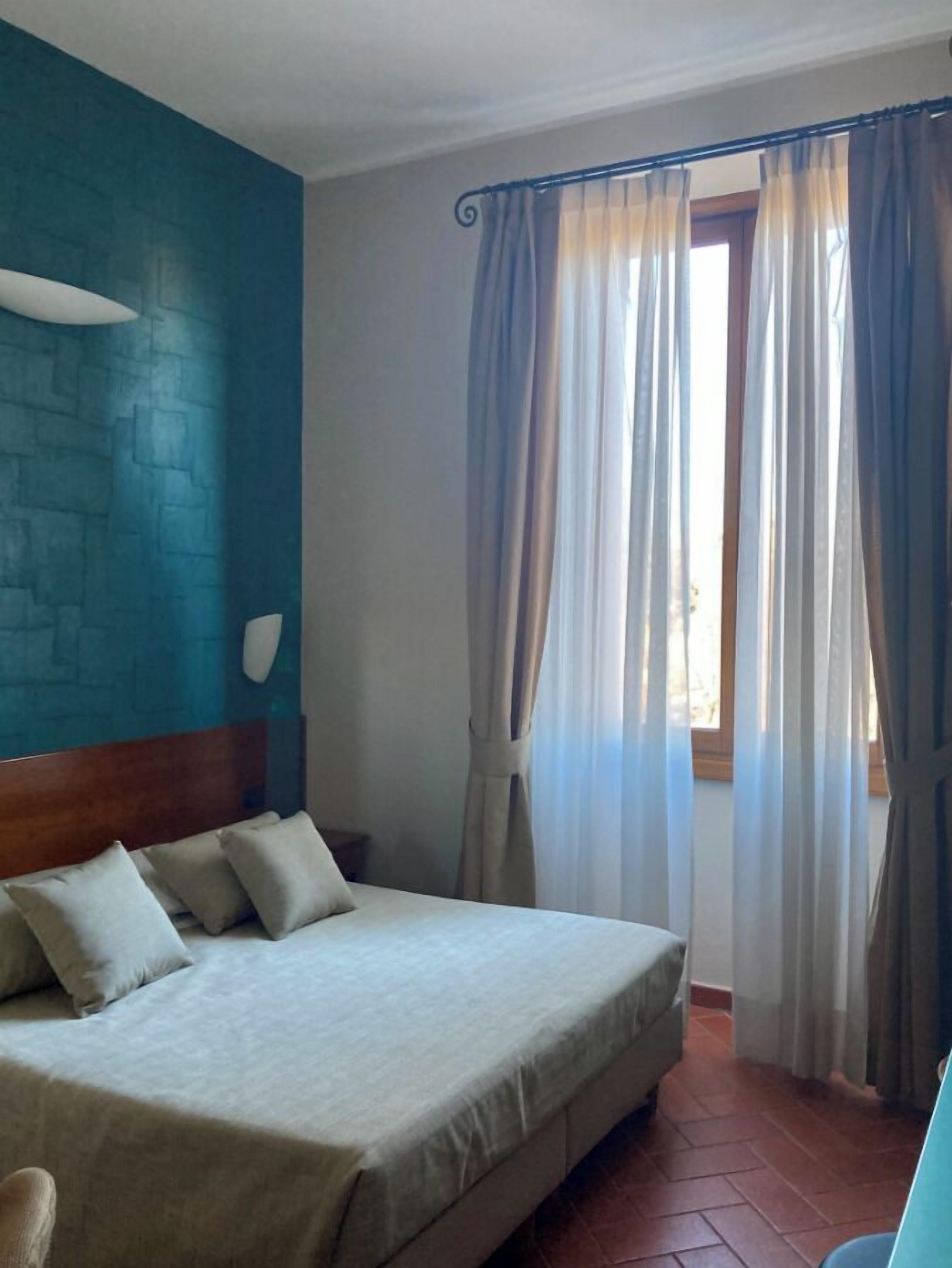 Una camera d'albergo con un letto, una testiera, una parete con motivo decorativo e una finestra con tende.
