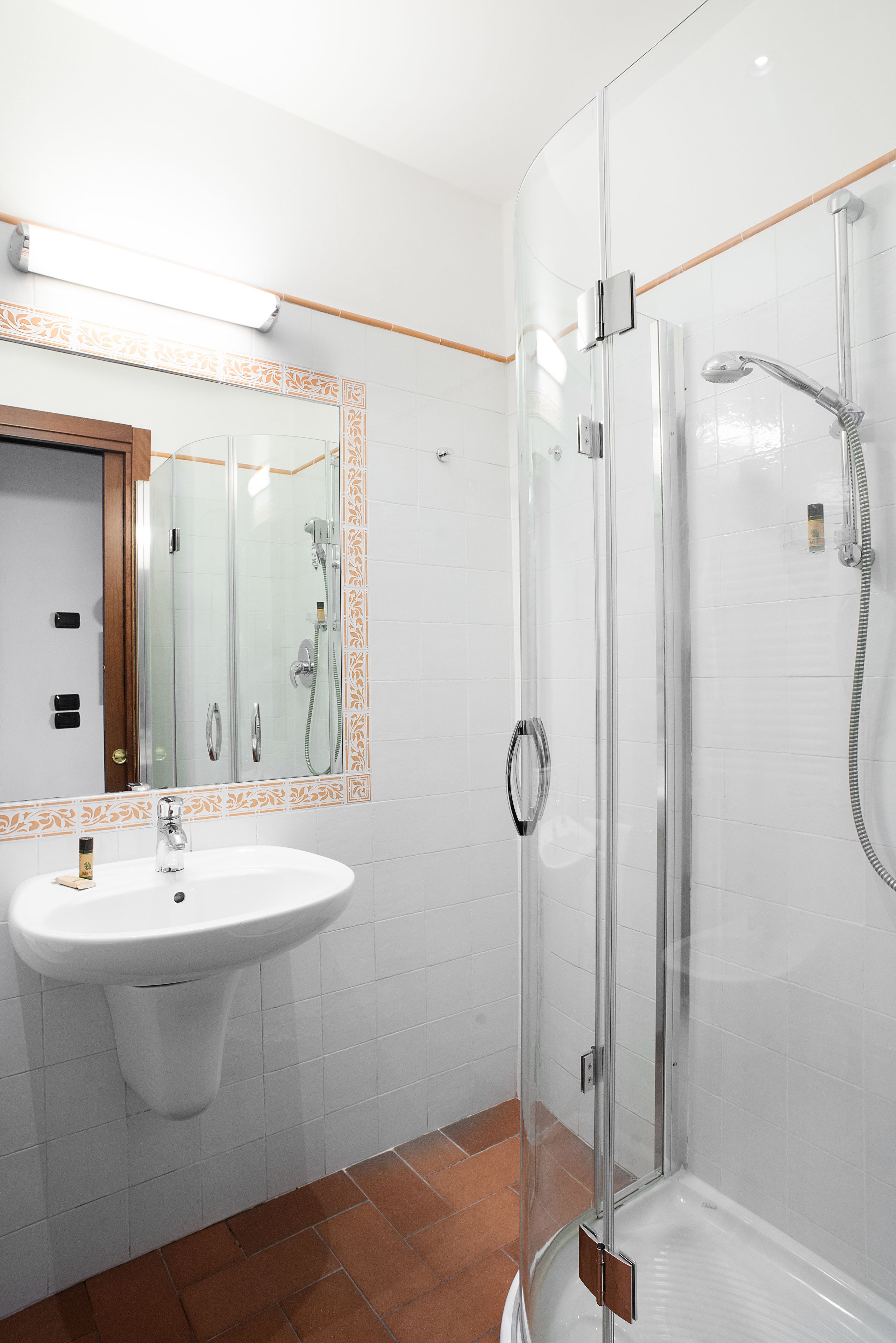 Een moderne badkamer met een douchecabine van glas, een wit wastafelmeubel met een spiegel erboven en een betegelde vloer.