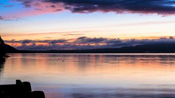 A calm lake at sunset with a silhouette of a dock and distant mountains.