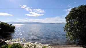A lakeside view with a sandy beach, clear water, and distant mountains.
