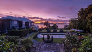 A residential property with a swimming pool, garden, and a view of a lake at sunset.