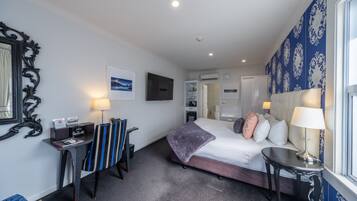 A hotel room with a bed, bedside table, desk, chair, and a large window.
