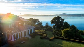 Ein Haus mit einem großen Wintergarten, einem gepflegten Rasen und Blick auf einen stillen See.