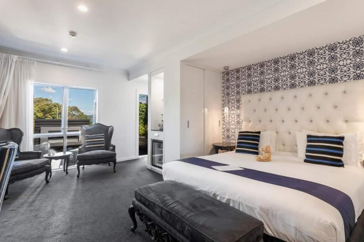 Una habitación de hotel moderna con una cama grande, una zona de estar con dos sillones, una mesita y vistas a zonas verdes.