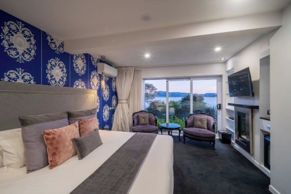 Una habitación de hotel con una cama grande, dos sillones, una mesita y un televisor.