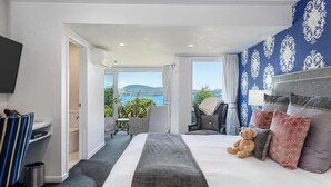 A hotel room with a large bed, a teddy bear, and a view of the sea.