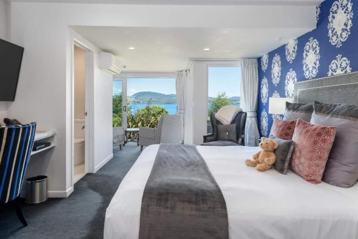 Un cuarto de hotel con una cama grande, un oso de peluche y vista al mar.