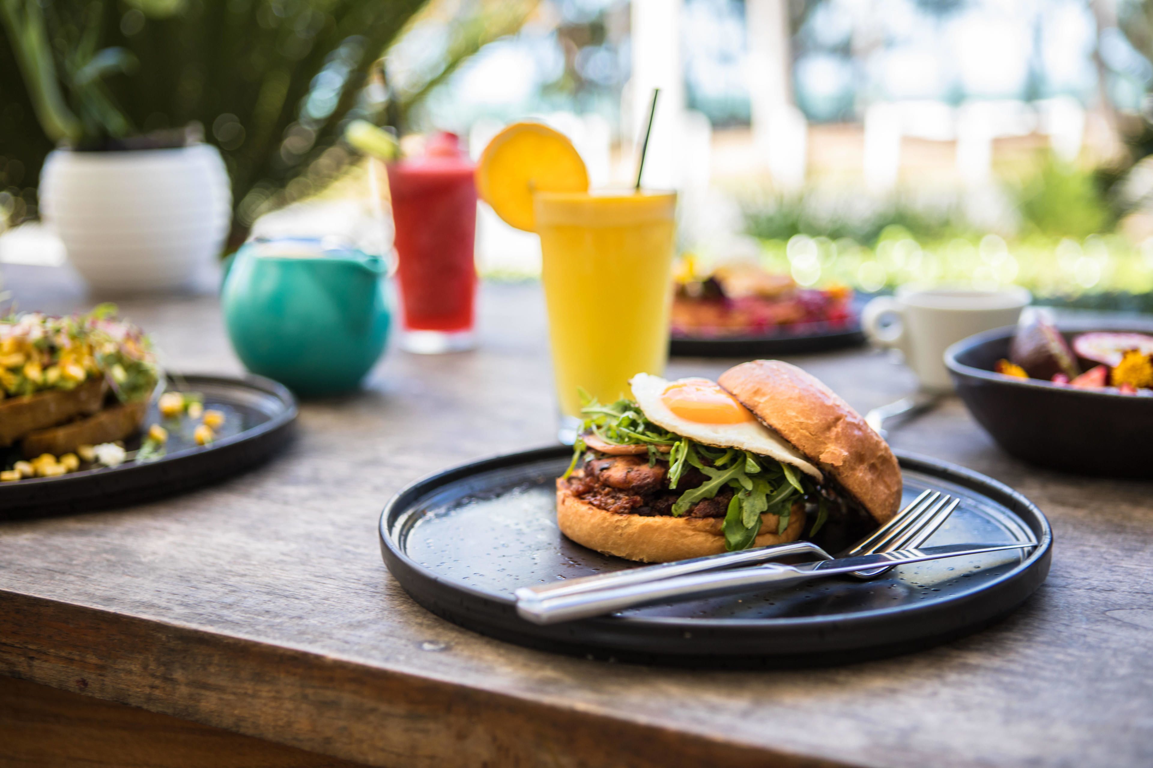A dining table with a burger, a drink, and a bowl of fruit.