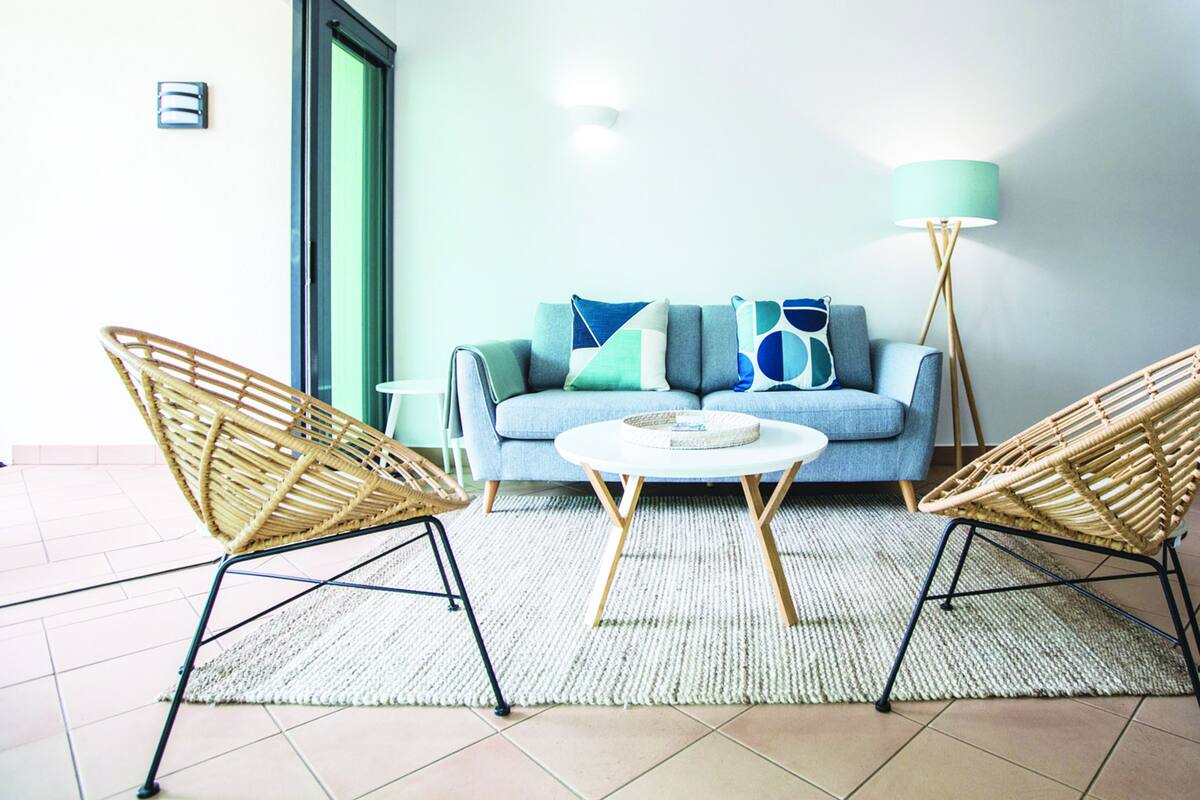Ein Wohnzimmer mit einer Couch, zwei Korbstühlen, einem runden Couchtisch und einer Stehlampe.