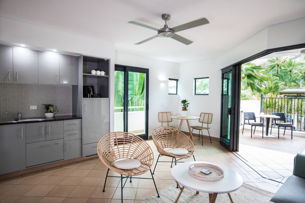Eine moderne Küche mit grauen Schränken, ein Essbereich mit Korbstühlen und ein Balkon mit Sitzgelegenheit.