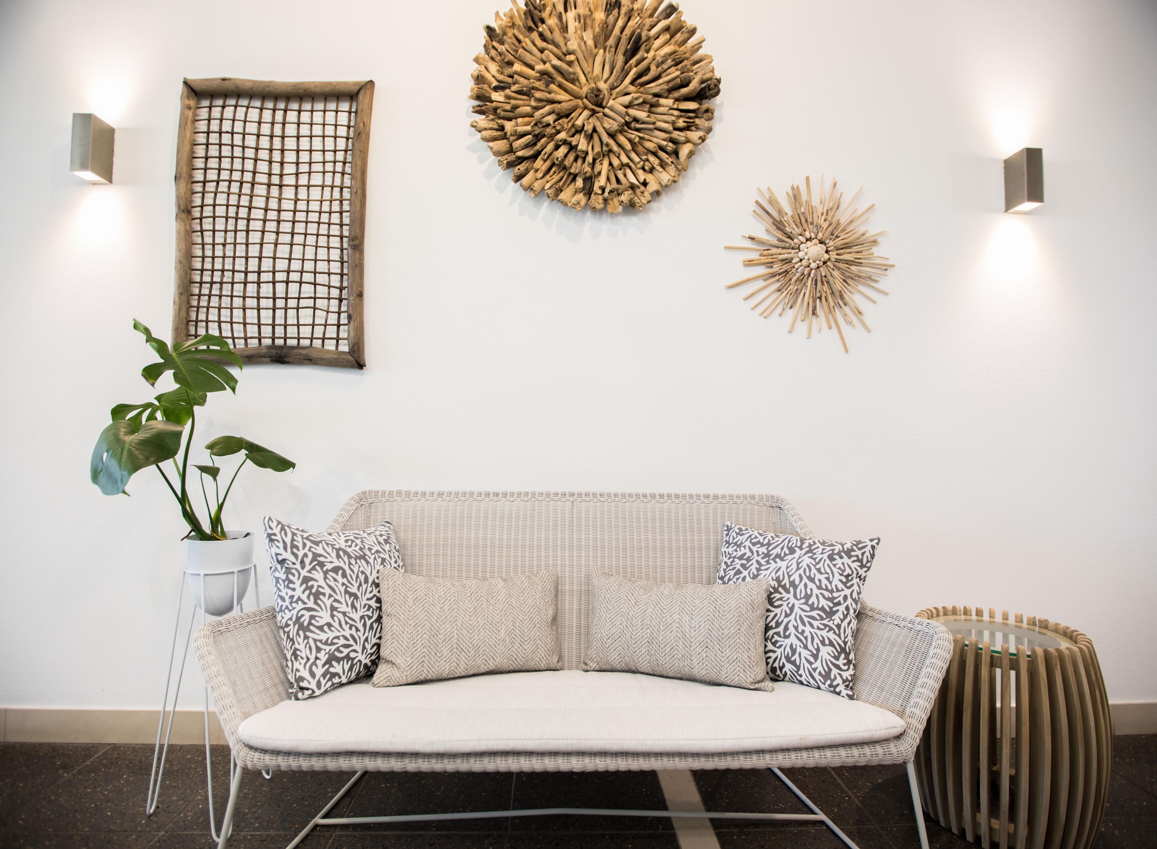 A modern living room with a wicker sofa, patterned cushions, a potted plant, and decorative wall art.
