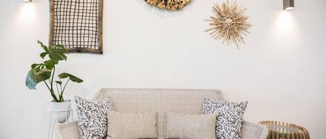 A modern living room with a wicker sofa, patterned cushions, a potted plant, and decorative wall art.