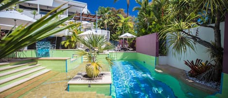 Una piscina al aire libre, sombrillas, sillones reclinables de piscina