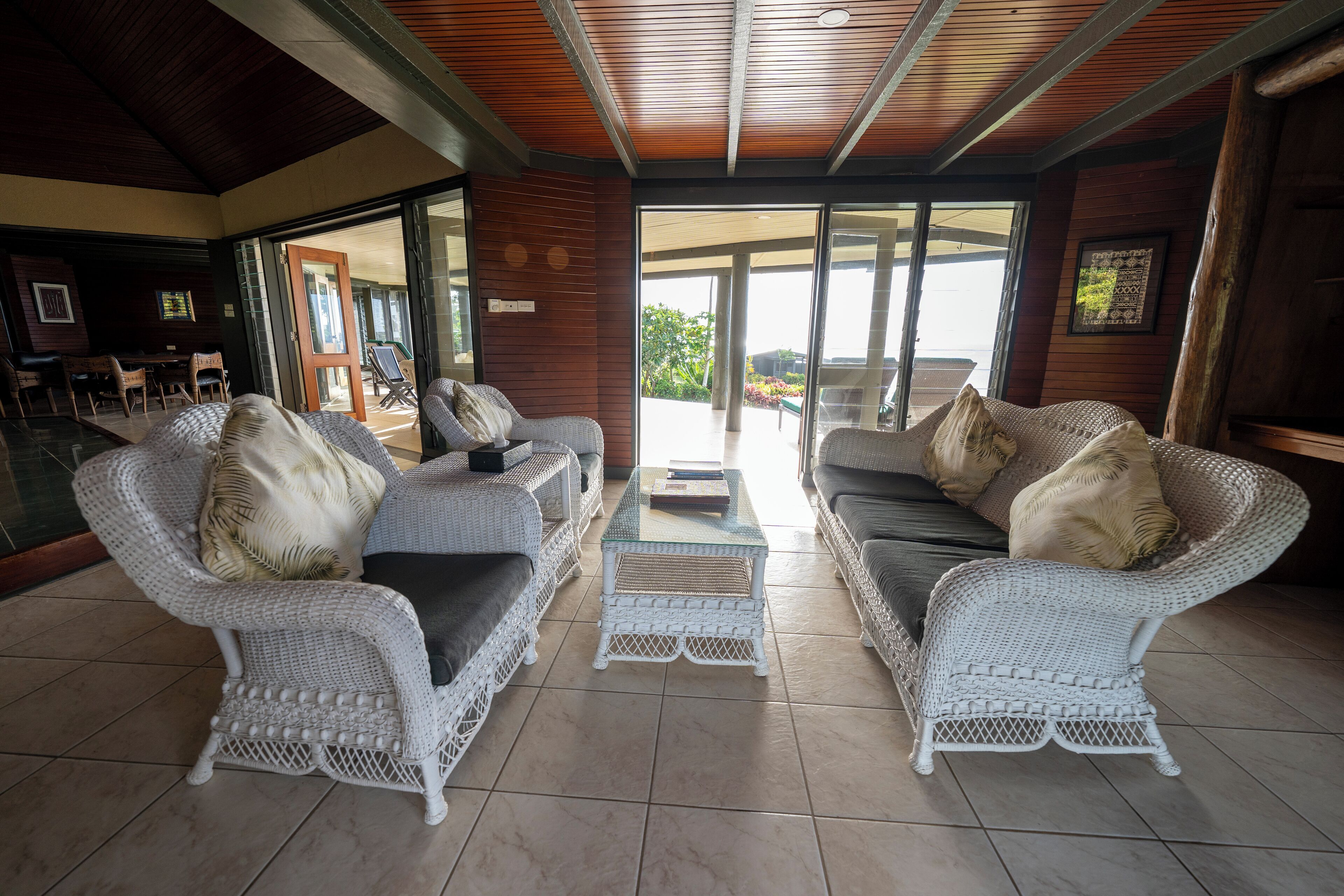 A spacious living area with wicker furniture, a glass coffee table, and a view through a glass door to an outdoor patio.