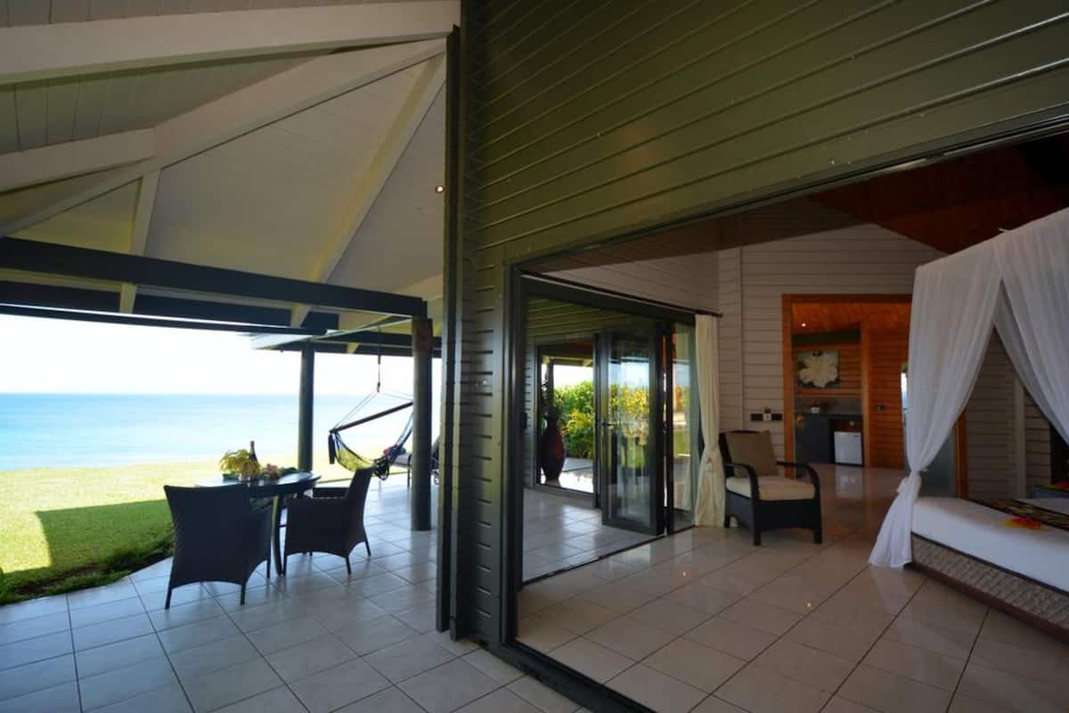 A modern villa with a glass door leading to a terrace with a view of the sea. Inside, there is a cozy sitting area with a sofa and a dining table.