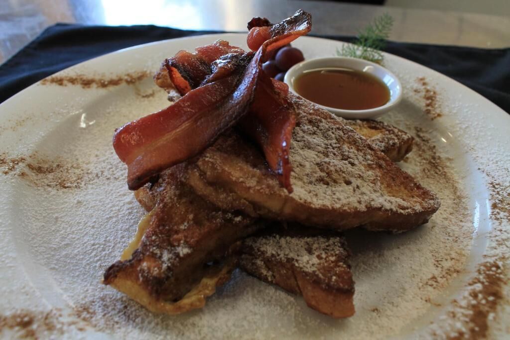 A plate with French toast, bacon, and a small cup of syrup.