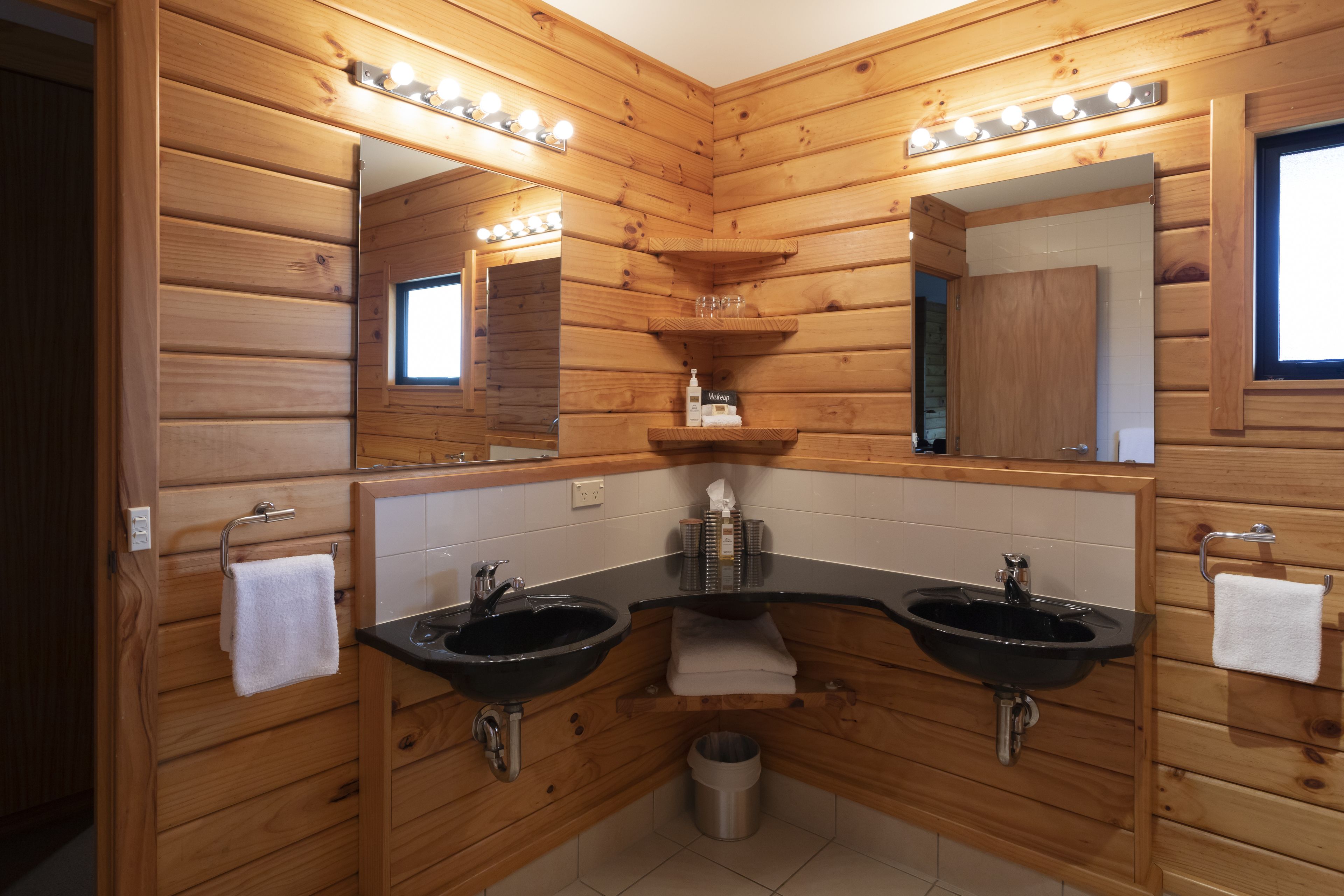 Une salle de bain de style rustique, avec des murs en bois, deux lavabos, un meuble-lavabo, un miroir et une fenêtre.