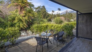 A patio with a table and chairs, surrounded by lush greenery and a view of snow-capped mountains.
