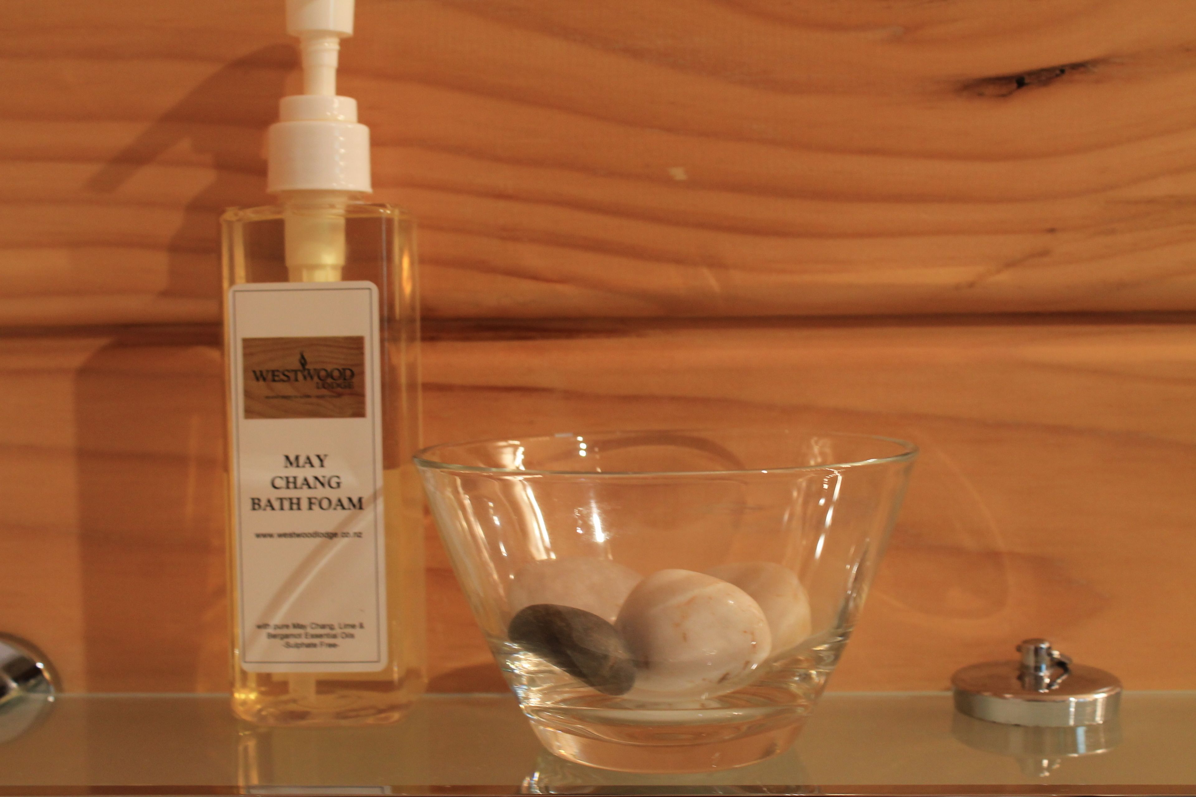 Un tazón de vidrio transparente con espuma de baño y una botella de Espuma de Baño May Chang Westwood.