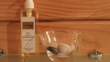 Un tazón de vidrio transparente con espuma de baño y una botella de Espuma de Baño May Chang Westwood.