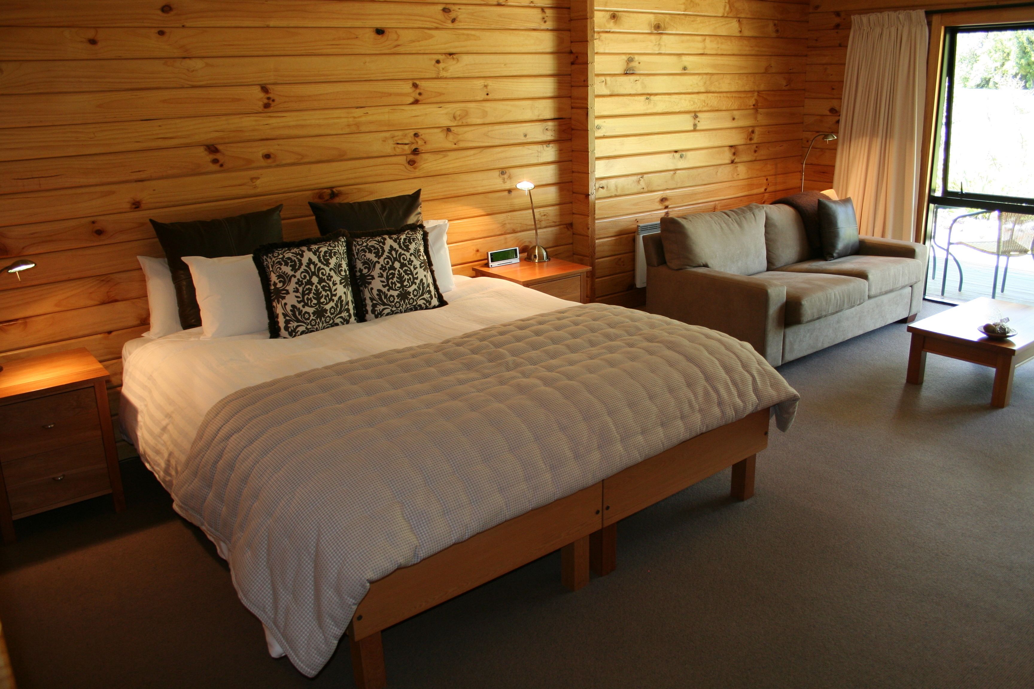 Un dormitorio con paneles de madera, una cama grande, un sofá y una mesita.