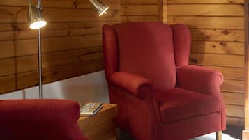 A wooden cabin interior with a red armchair, a floor lamp, and a book on a wooden table.