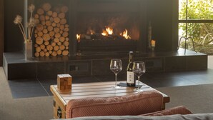 A modern living room with a fireplace, a wooden coffee table with wine glasses and a bottle, and a stack of firewood.