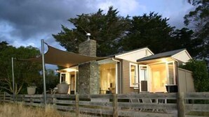 Una casa a due piani con un camino in pietra, una recinzione in legno e un ombrellone grande.
