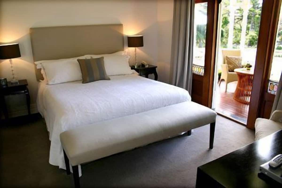 Un grand lit avec une banquette, deux tables de chevet et une vue sur un espace extérieur aménagé avec une table et des chaises.