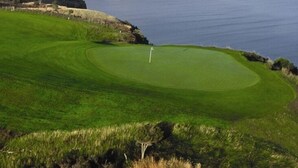 Un campo da golf con un bastoncino di bandiera sul green, circondato da scogliere e un corpo d'acqua.