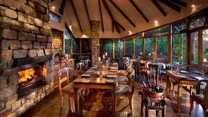 A dining area with a stone fireplace, wooden tables, and chairs.