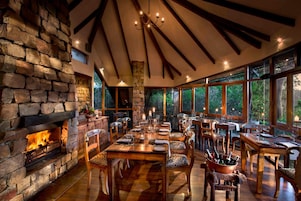 Un comedor con chimenea de piedra, mesas y sillas de madera.