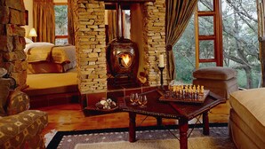 A cozy room with a stone fireplace, a chessboard, and a bed with a view of trees.