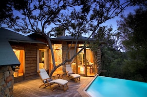 Una cabaña de troncos con piscina, terraza de madera y zona de estar al aire libre.