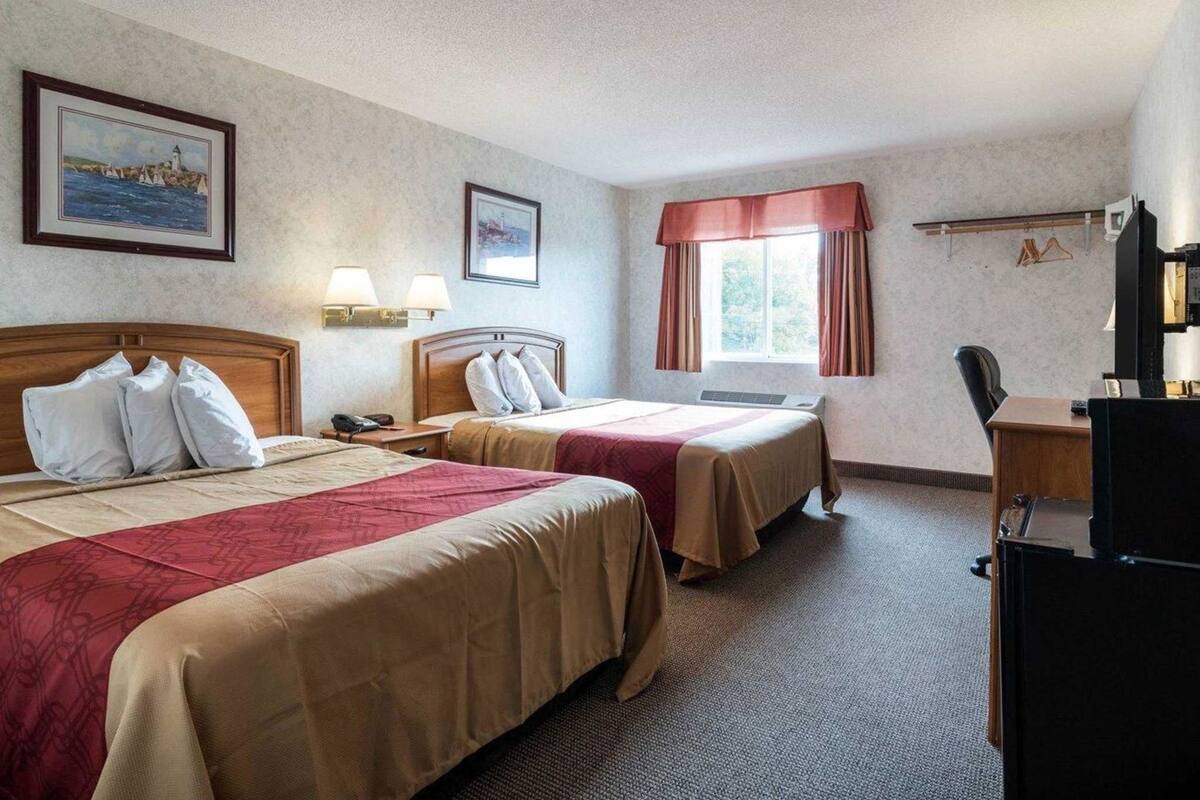 A hotel room with two beds, a desk, a chair, a TV, and a window with curtains.