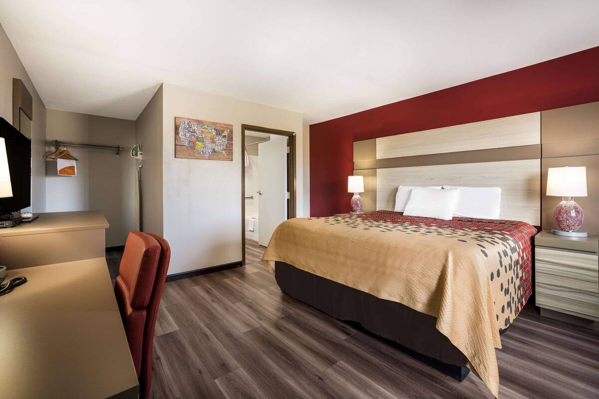 A hotel room with a bed, desk, chair, and a red accent wall.
