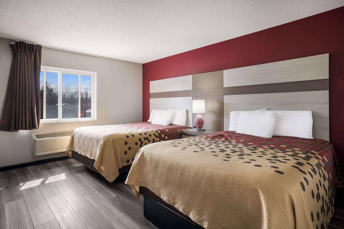 A hotel room with two beds, a large window with curtains, a radiator, and a view of the outside.