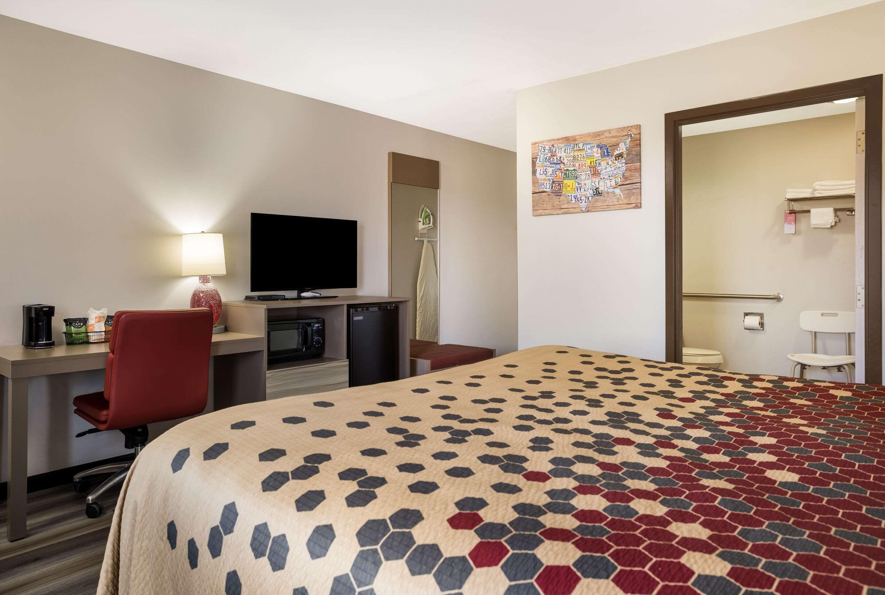 A hotel room with a bed, desk, chair, TV, and a bathroom visible through an open door.